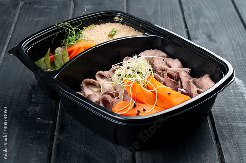 Ham with couscous and vegetables in containers on a black wooden background. Takeaway. Diet and healthy food.