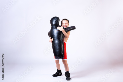 Cheerful sports boy in wrestling tights and wrestling holds a sporting dummy in his hands for training and handling techniques from various martial arts on a fir-tree isolated background.  © Виталий Сова