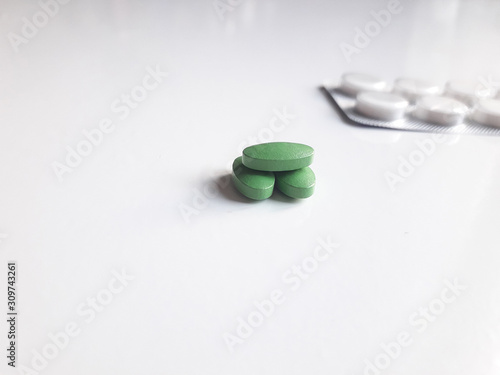 Miraculous and pernicious means. Hill of green pills in the focus in the foreground and blister pack with white tablets in the unfocused background