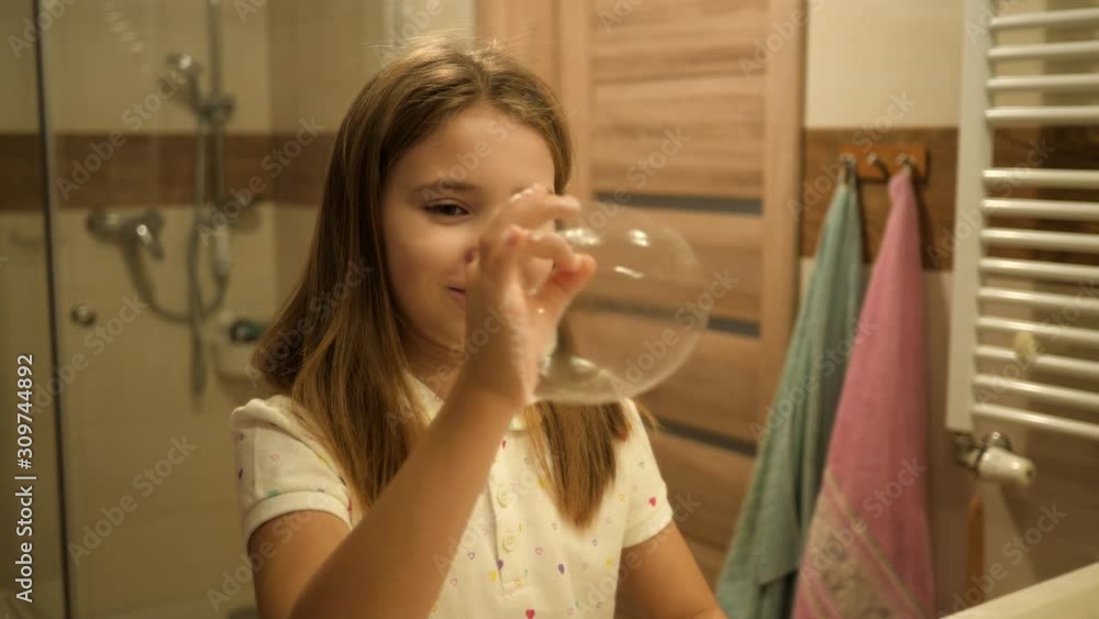 After washing hands cute kid girl play make soap bubbles in bathroom in front of mirror having fun in pajamas in the morning After washing hands cute kid girl play make soap bubbles in bathroom in front of mirror having fun in pajamas in the morning