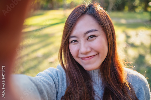 Portrait image of a happy beautiful asian woman making selfie photo in park