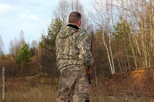 A hunter in protective clothing with a firearm observes the environment during the hunt.