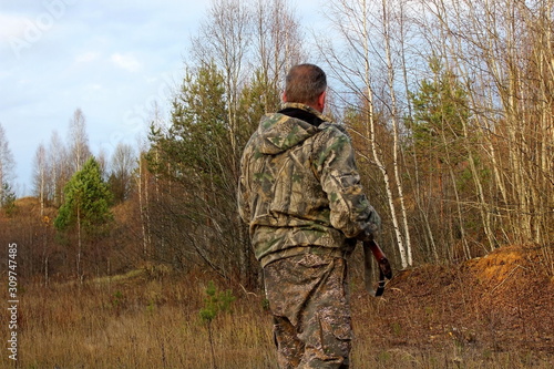 A hunter in protective clothing with a firearm observes the environment during the hunt.