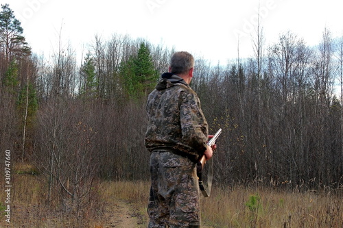 A hunter in protective clothing with a firearm observes the environment during the hunt.