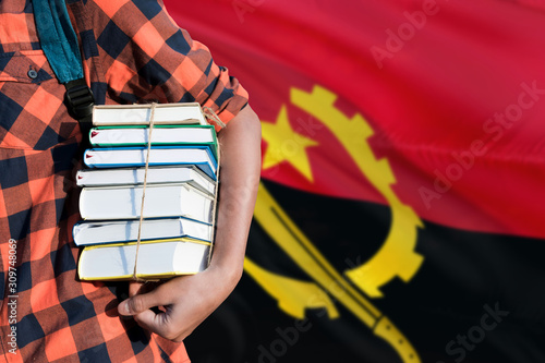 Angola national education concept. Close up of teenage student holding books under his arm with country flag background.