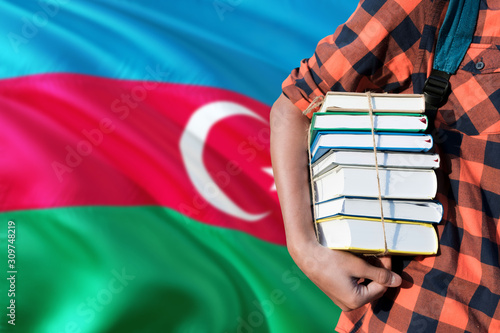Azerbaijan national education concept. Close up of teenage student holding books under his arm with country flag background. © sezerozger