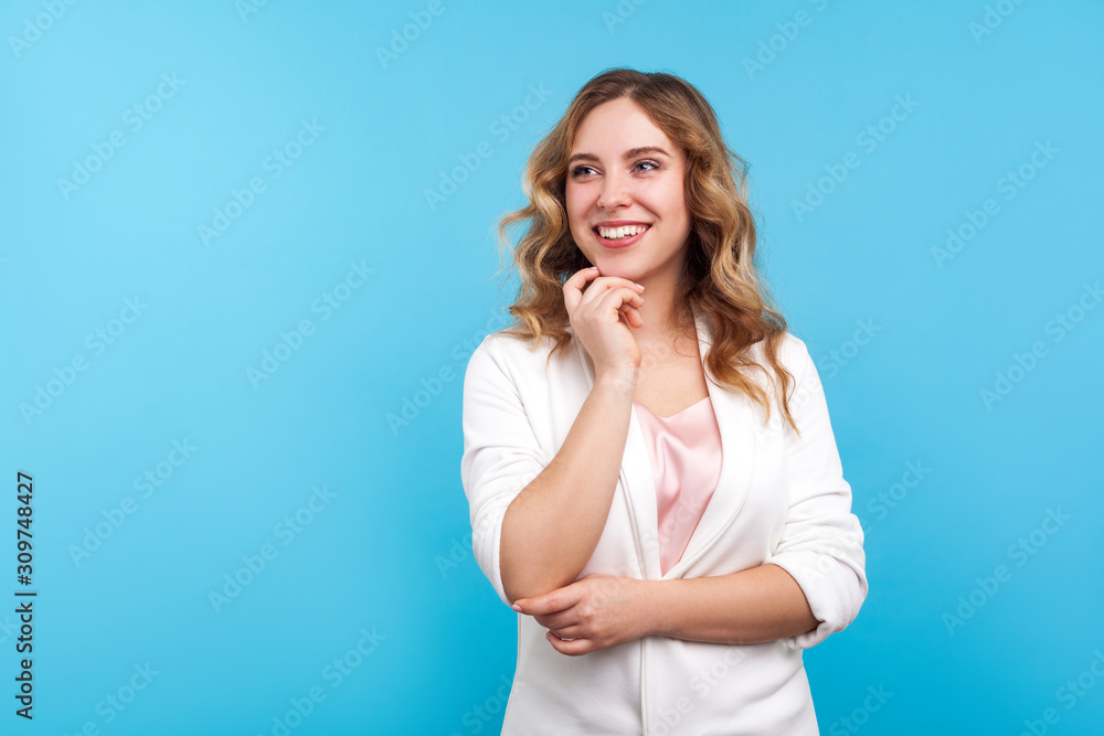 Portrait of amazing happy woman with wavy hair in white jacket touching chin while thinking, dreaming with joyous smiling face, pleasant fantasy, positive hopes. indoor studio shot, blue background Portrait of amazing happy woman with wavy hair in white jacket touching chin while thinking, dreaming with joyous smiling face, pleasant fantasy, positive hopes. indoor studio shot, blue background