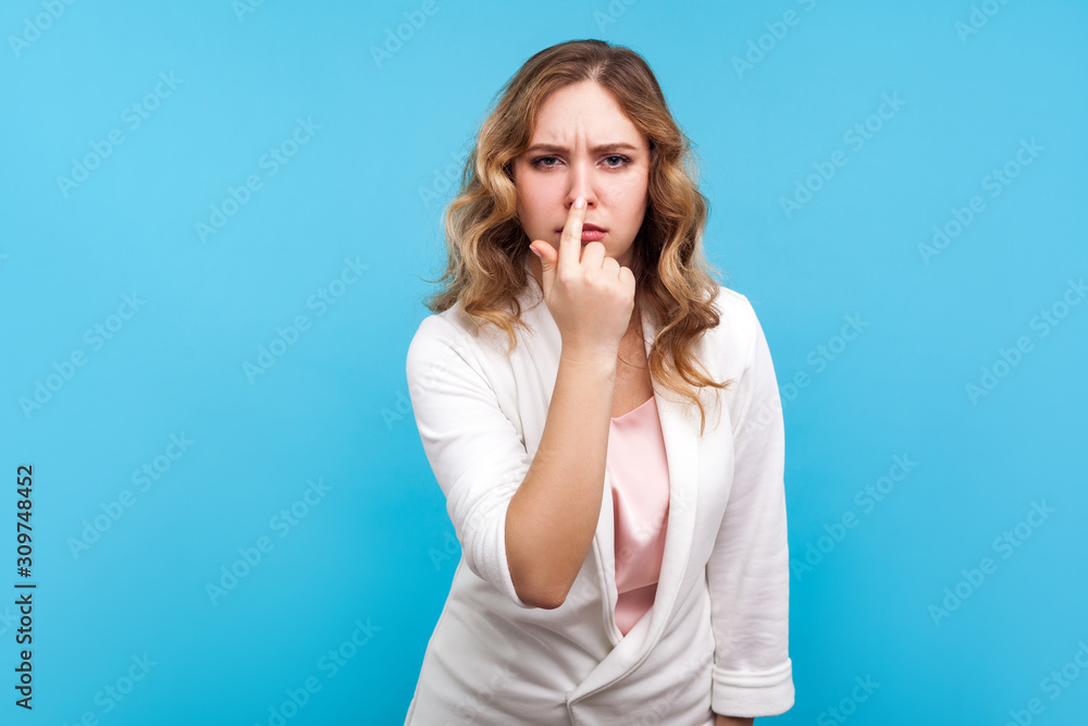 You are liar. Portrait of upset woman with wavy hair in white jacket touching nose showing lie gesture and frowning face, having suspicious about falsehood, dishonesty. studio shot, blue background You are liar. Portrait of upset woman with wavy hair in white jacket touching nose showing lie gesture and frowning face, having suspicious about falsehood, dishonesty. studio shot, blue background
