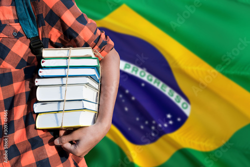 Brazil national education concept. Close up of teenage student holding books under his arm with country flag background.