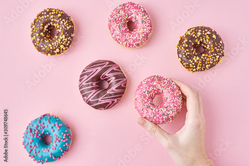 Woman hand take color donut on a pink background. Creativity minimalism style food concept, top view