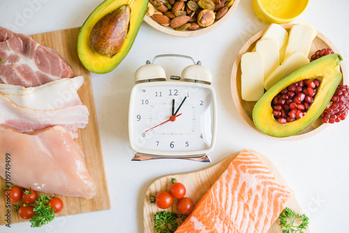 Intermittent fasting and Healthy food. Concept.Alarm clock and Keto diet food ingredients on white table.Ketogenic mean Low carb and High fat. photo