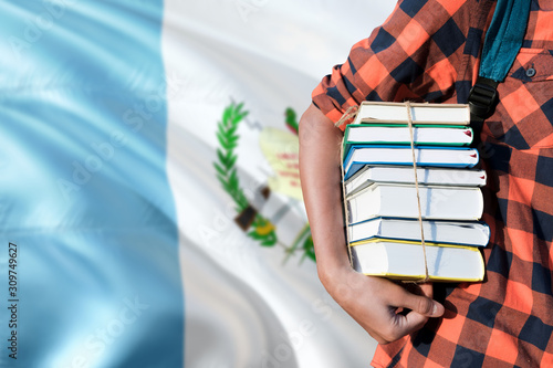 Guatemala national education concept. Close up of teenage student holding books under his arm with country flag background. © sezerozger