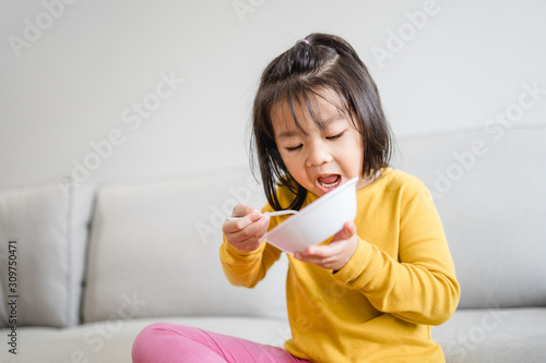 Hungry little asian girl eating rice with salmon teriyaki and watching TV in sofa at home.Happy meal and Delicious asian food concept.