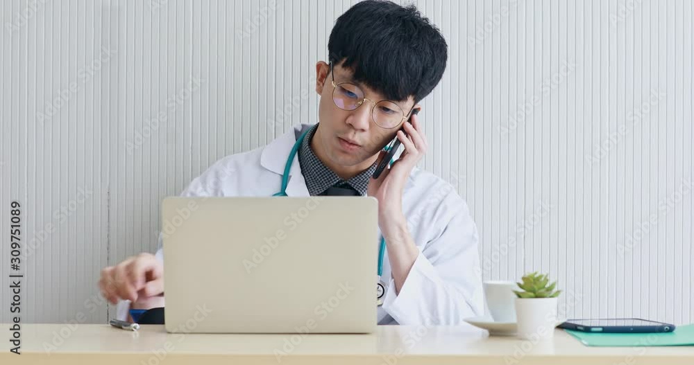 Asian handsome male doctor checked the information from the notebook computer and called the patient to check the patient's condition. Asian handsome male doctor checked the information from the notebook computer and called the patient to check the patient's condition.