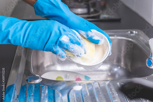 фотографія Close up of a man wearing a blue rubber glove was washing the cup with a dish washing liquid in the sink in the kitchen