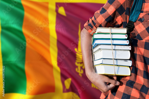 Sri Lanka national education concept. Close up of teenage student holding books under his arm with country flag background.
