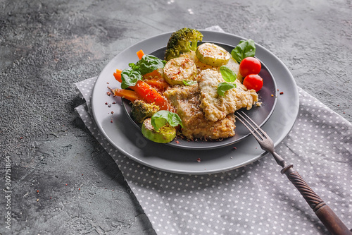 Cod with baked vegetables and fresh basil. Serving on a napkin on a gray concrete background. Healthy and tasty food. Traditional cuisine seafood