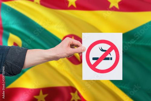 Grenada health concept. Hand holding paper with no smoking sign over national waving flag. Quit smoke theme.