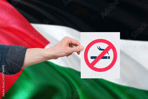 Palestine health concept. Hand holding paper with no smoking sign over national waving flag. Quit smoke theme.