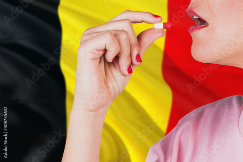 Belgium health care concept. Close-up of a woman taking vitamin capsule on national flag background.