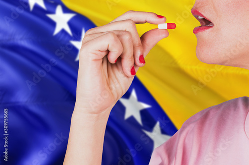 Bosnia Herzegovina health care concept. Close-up of a woman taking vitamin capsule on national flag background.