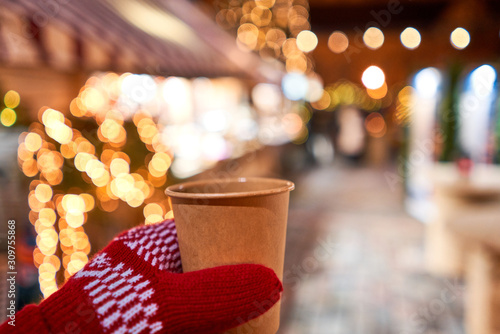 Hand holding a cup of mulled wine with blurred background of winter wonderland  a Christmas Market in European small city