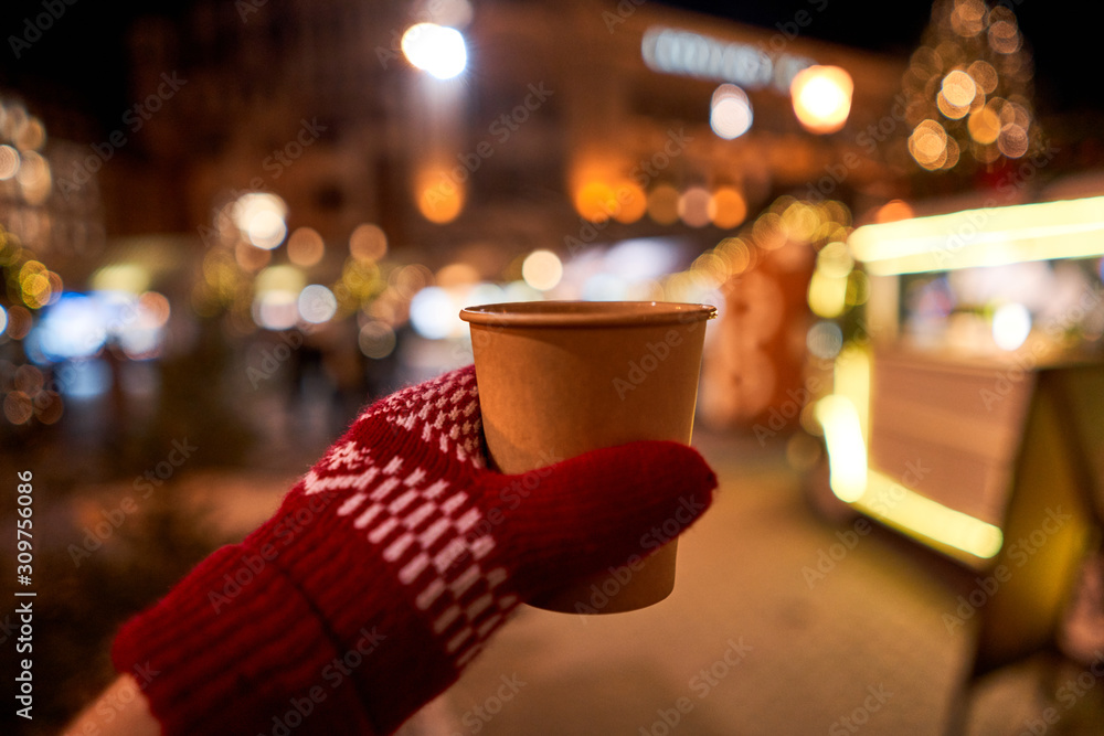 Hand holding a cup of mulled wine with blurred background of winter wonderland, a Christmas Market in European small city Hand holding a cup of mulled wine with blurred background of winter wonderland, a Christmas Market in European small city
