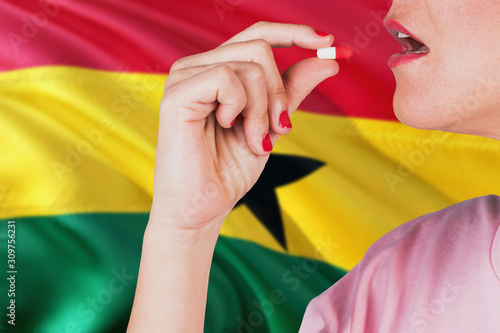 Ghana health care concept. Close-up of a woman taking vitamin capsule on national flag background.