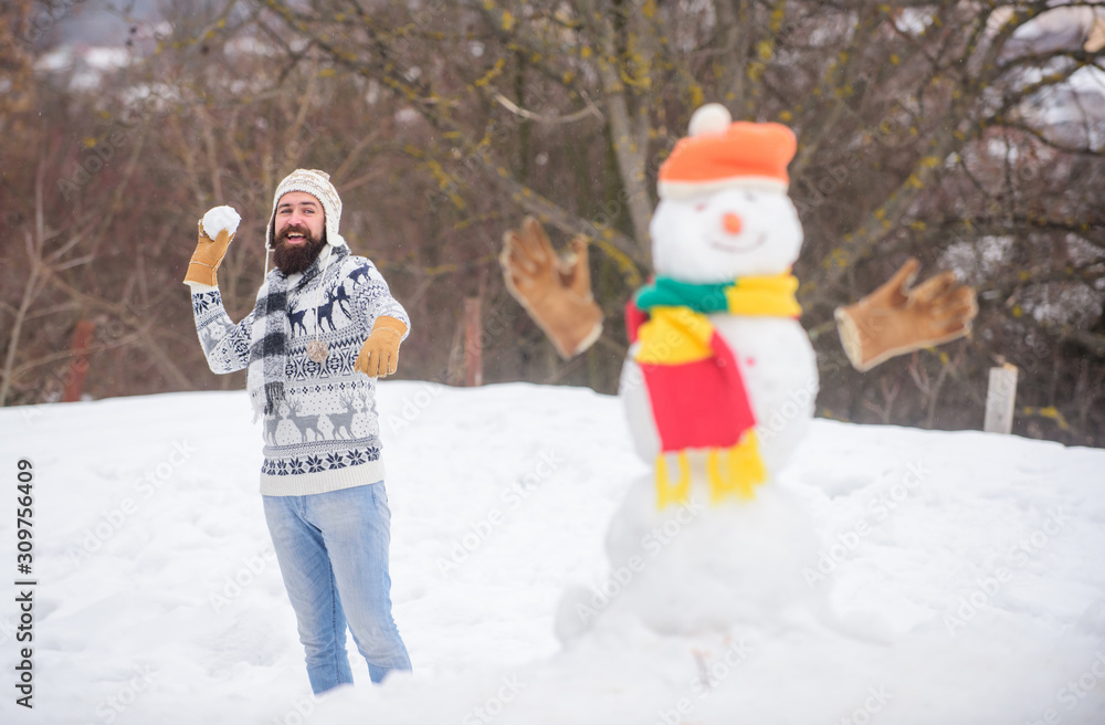 Let it snow. Christmas holidays. Active lifestyle. Snow games. Leisure on fresh air. Snowman and cheerful bearded hipster knitted hat and warm gloves play with snow outdoors. Have fun winter day