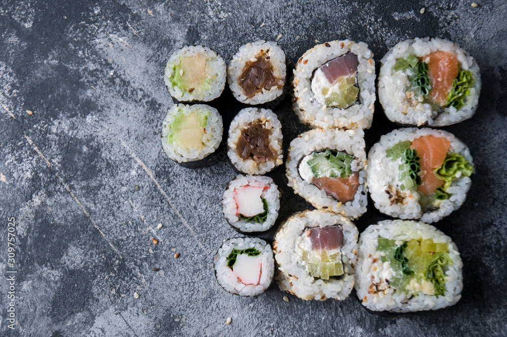 Different sushi on a dark textured background, fresh futomaki, uramaki and hosomaki. Different sushi on a dark textured background, fresh futomaki, uramaki and hosomaki.