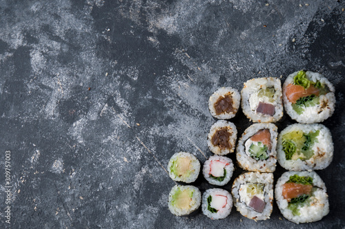 Different sushi on a dark textured background with place for text, fresh futomaki, uramaki and hosomaki.