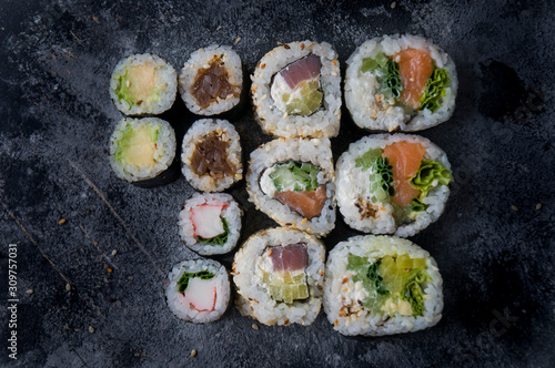 Different sushi on a dark textured background, fresh futomaki, uramaki and hosomaki.