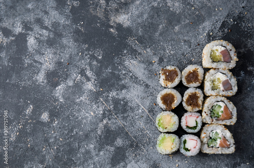 Different sushi on a dark textured background with place for text, fresh futomaki, uramaki and hosomaki.