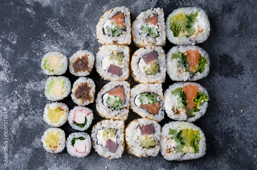 Different sushi on a dark textured background, fresh futomaki, uramaki and hosomaki.