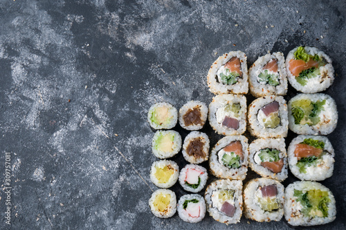 Different sushi on a dark textured background with place for text, fresh futomaki, uramaki and hosomaki.
