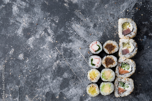 Different sushi on a dark textured background with place for text, fresh futomaki, uramaki and hosomaki.