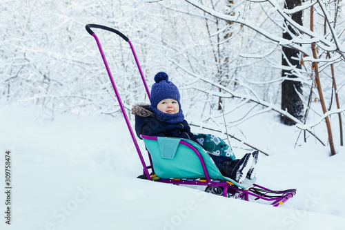 A little boy in a snowy winter forest, among the trees in hoarfrost sits in a sleigh