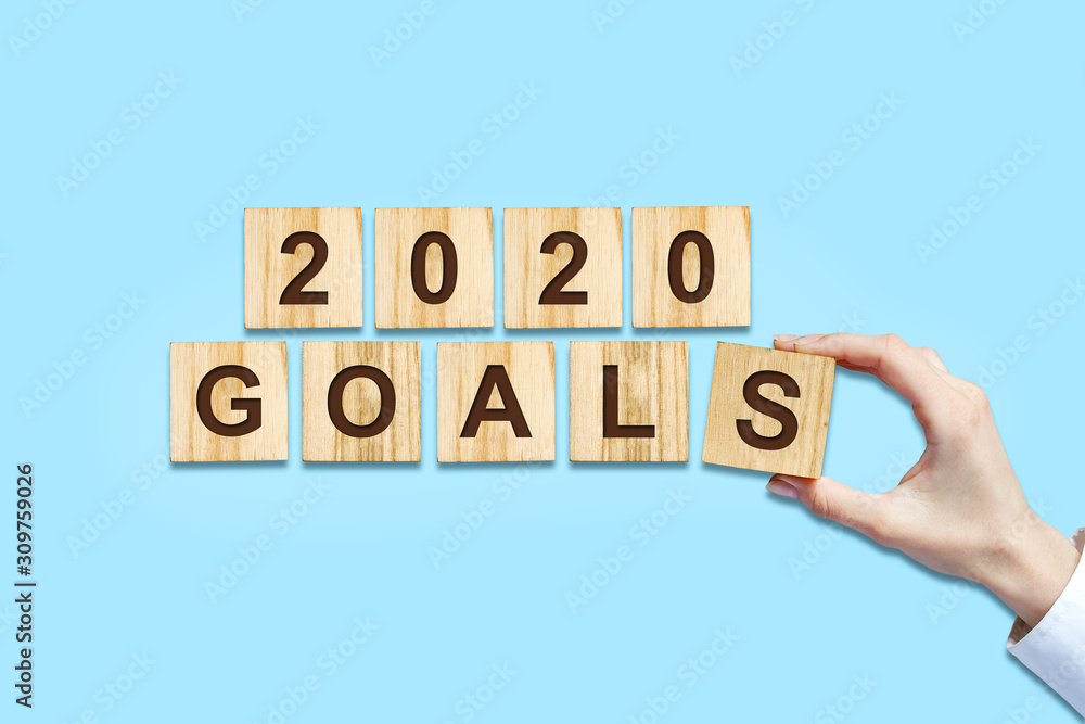 2020. Goals. Female hand makes up words from wooden blocks. Isolated on a blue background. New Year Goals Concept. 2020. Goals. Female hand makes up words from wooden blocks. Isolated on a blue background. New Year Goals Concept.