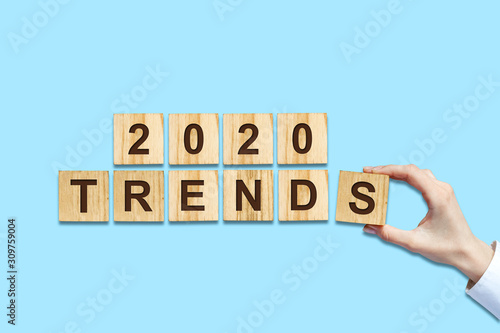 2020. Trends. Female hand makes up words from wooden blocks. Isolated on a blue background. New Year Trends Concept. B