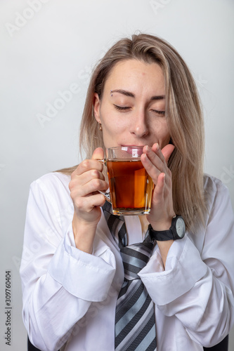 A blond woman in a white shirt and tie is drinking tea. There is a break in the train.