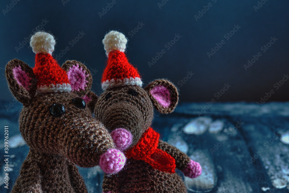 Lovely handcrafted amigurumi rats with christmas hats and red scarves standing near on the blue background. New Year 2020 concept