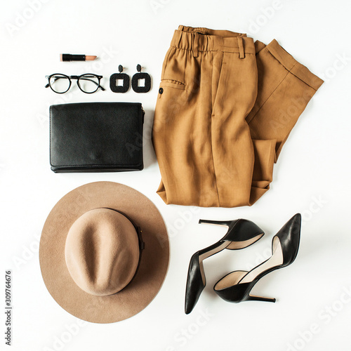 Women fashion clothes, accessories on white background. Flat lay, top view minimal trendy lifestyle collage. Pants, high-heel shoes, glasses, hat, purse bag, earrings. Fashion blogger concept.