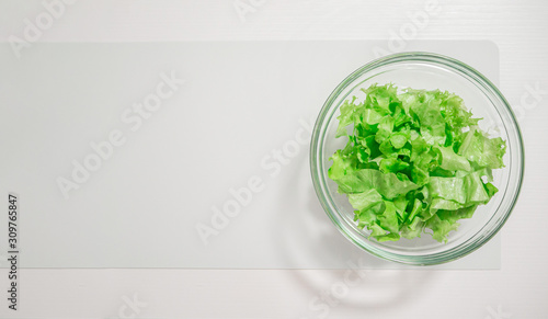 Transparent bowl with green salad on a white table, top view, copy space