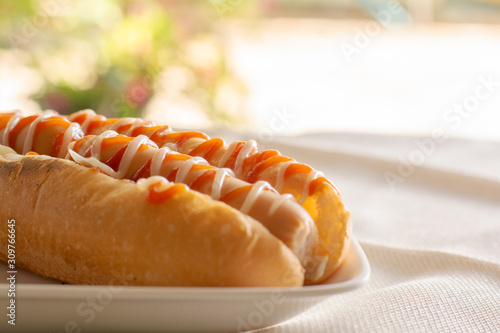 Hot dog with bun and ketchup, mayonnaise on white plate. Sausage sandwich for lunch. Fast food concept.