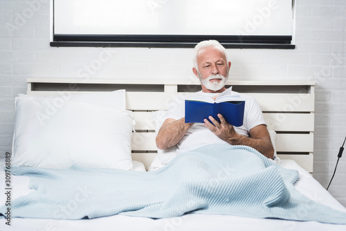 Senior man at home reading book in bed before sleep.