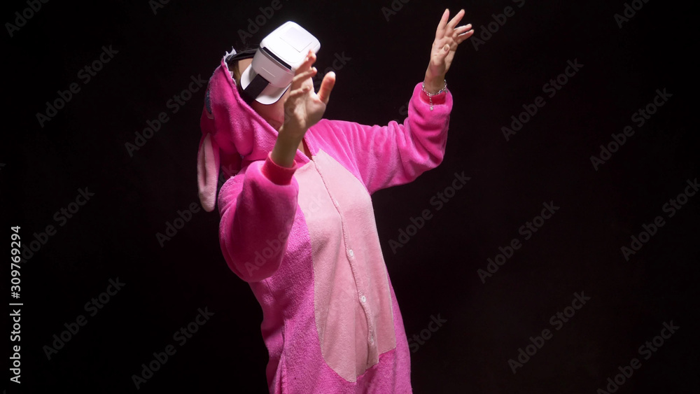 girl in pink pajamas kigurumi in VR glasses on a black background. pajama party girl in pink pajamas kigurumi in VR glasses on a black background. pajama party