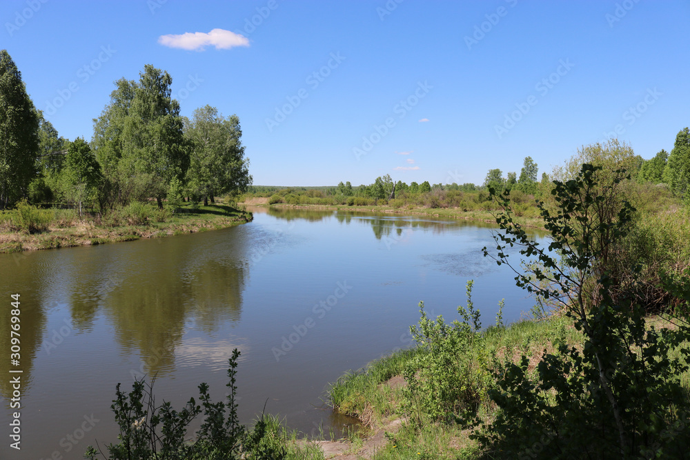 Summer landscape - A calm flat river among fields and birch groves under a blue sky. Cloudless summer weather. Summer landscape - A calm flat river among fields and birch groves under a blue sky. Cloudless summer weather.