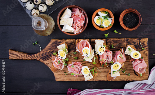 Bruschetta with prosciutto/jamon traditional Italian antipasto. Delicious snack with bread, brie cheese and quails eggs. Health food, tapas. Top view, copy space
