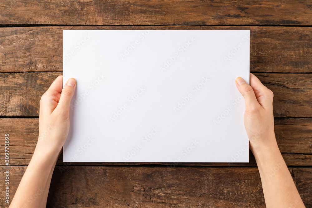 Overhead shot of female hands holding empty paper sheet on rustic wooden background Overhead shot of female hands holding empty paper sheet on rustic wooden background