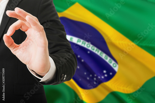 Brazil acceptance concept. Elegant businessman is showing ok sign with hand on national flag background.